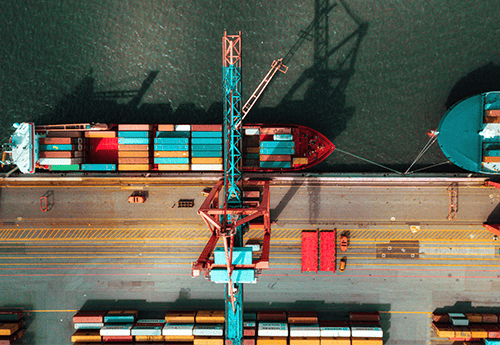 aerial view of a crane loading shipping containers onto a freight vessel in an industrial port